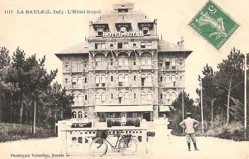 Cycliste de dos qui regarde l'hôtel, vélo posé contre la barrière